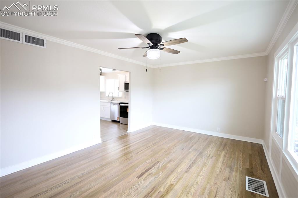 Unfurnished room with ornamental molding, light wood-style flooring, and ceiling fan