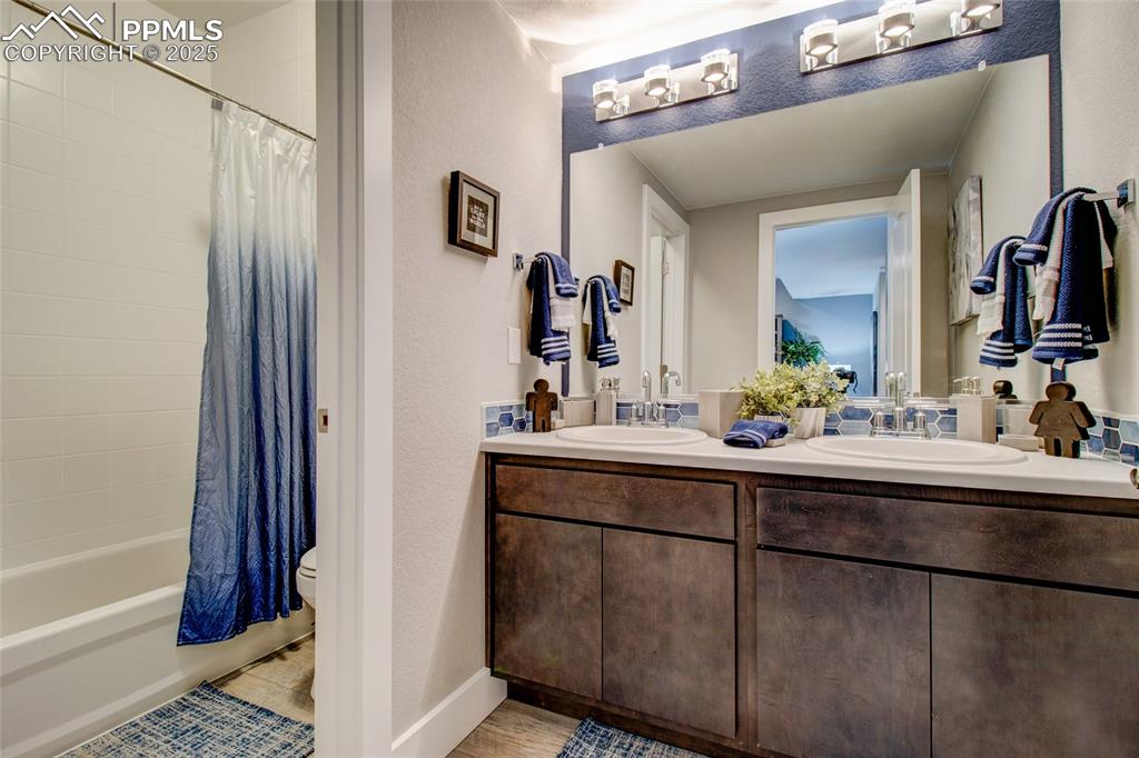 Bathroom with double vanity, shower / bath combo, and a textured wall