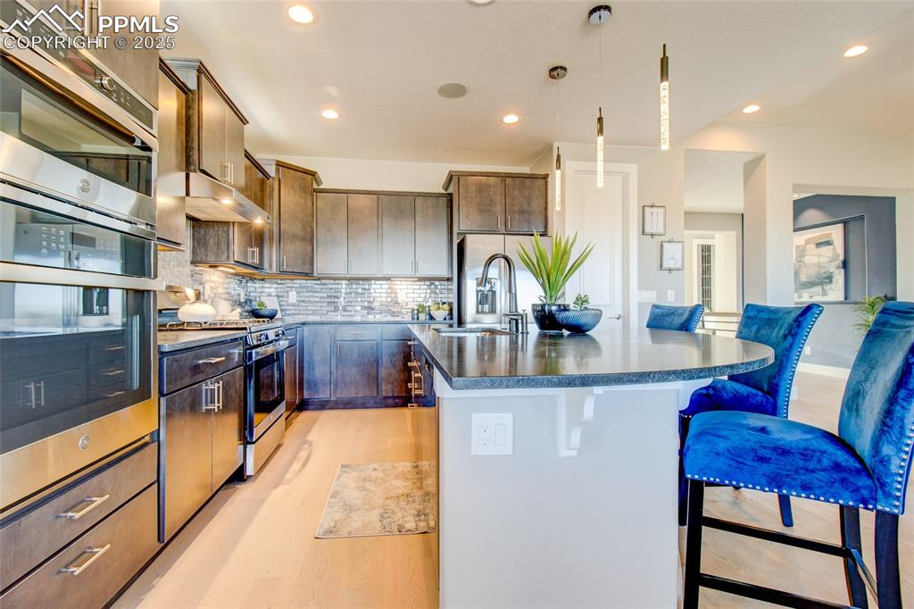 Kitchen with appliances with stainless steel finishes, a kitchen bar, dark countertops, an island with sink, and under cabinet range hood