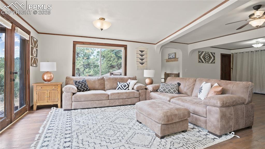 Living area featuring wood finished floors, healthy amount of natural light, ornamental molding, and ceiling fan