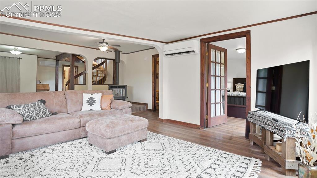 Living area with a wall mounted air conditioner, arched walkways, a wood stove, wood finished floors, and a ceiling fan