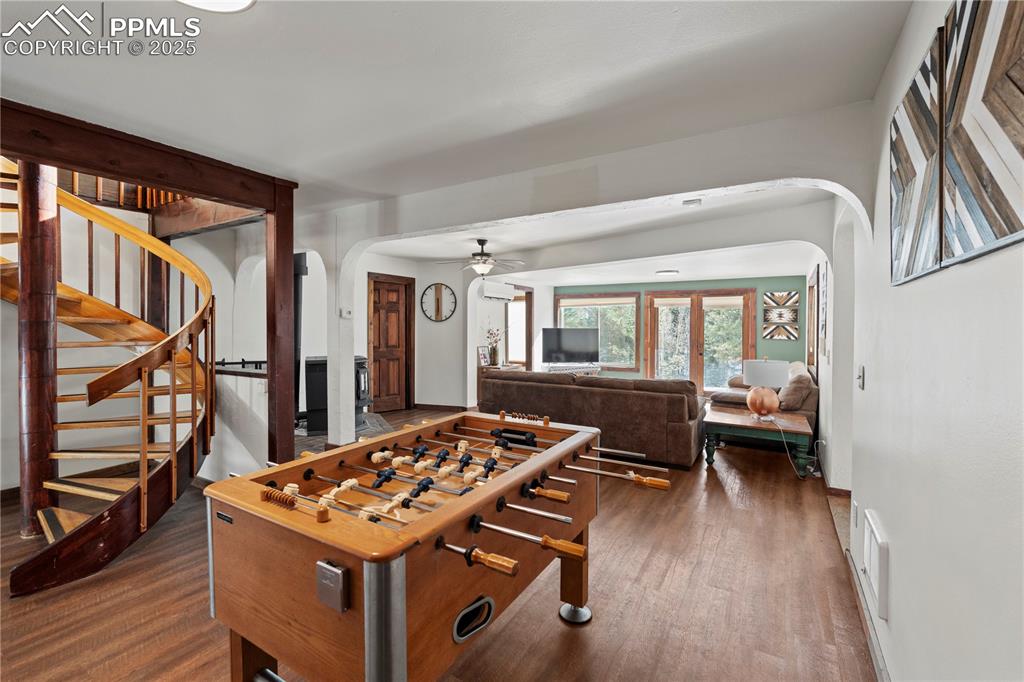 Rec room featuring arched walkways, dark wood-style floors, a ceiling fan, and baseboards