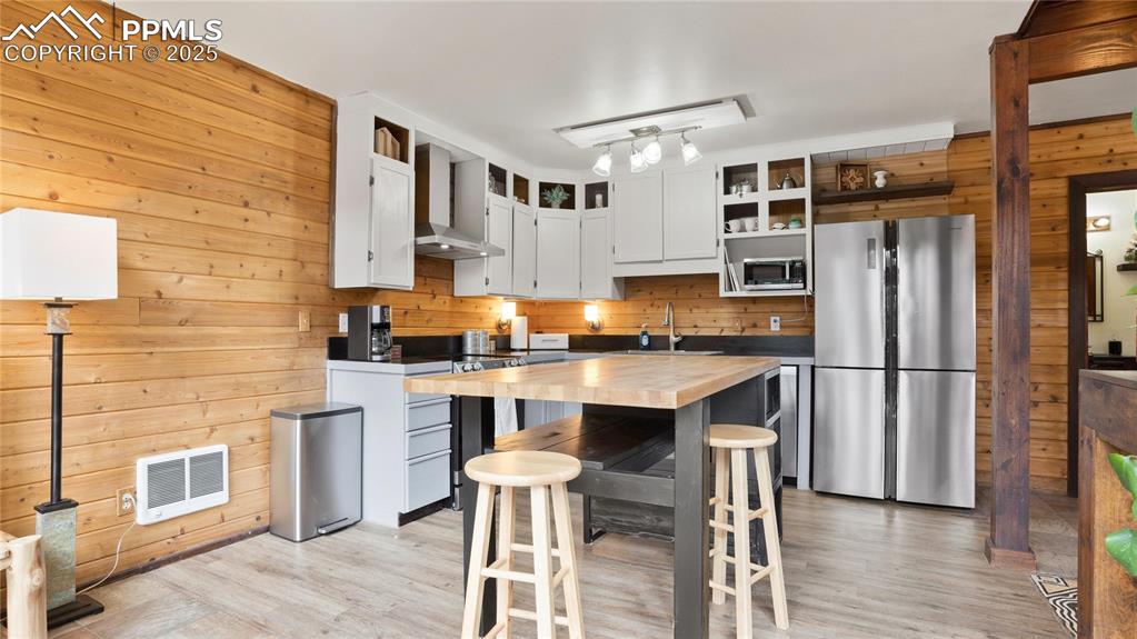 Kitchen with appliances with stainless steel finishes, butcher block counters, wooden walls, wall chimney range hood, and a sink