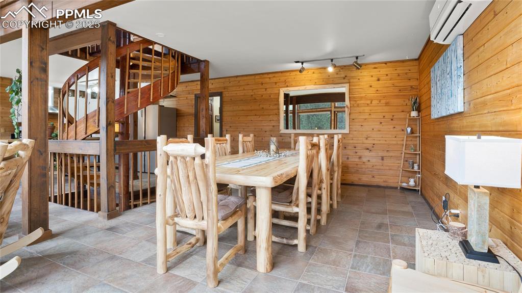 Dining space featuring rail lighting, wood walls, a wall mounted air conditioner, stone finish flooring, and stairway