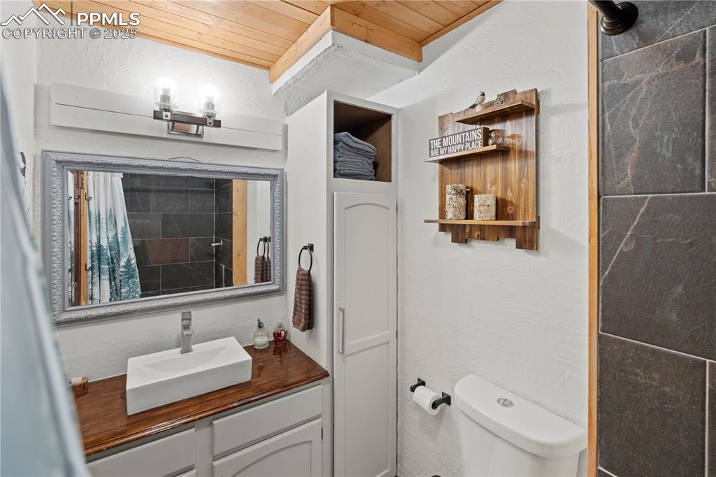 Full bathroom with wood ceiling, vanity, toilet, a textured wall, and a shower with curtain