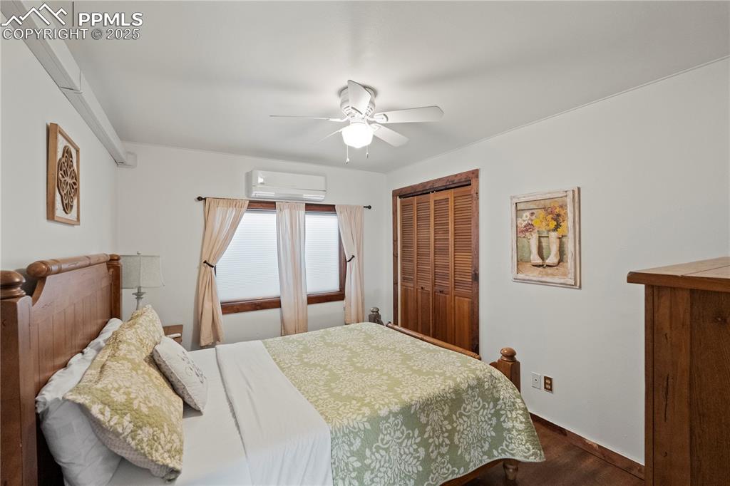 Bedroom with an AC wall unit, a closet, ceiling fan, dark wood-style flooring, and baseboards