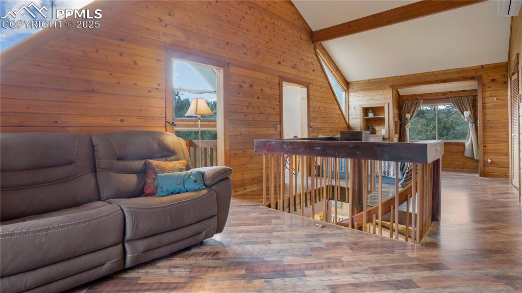 Living room featuring wood walls, wood finished floors, beamed ceiling, and high vaulted ceiling
