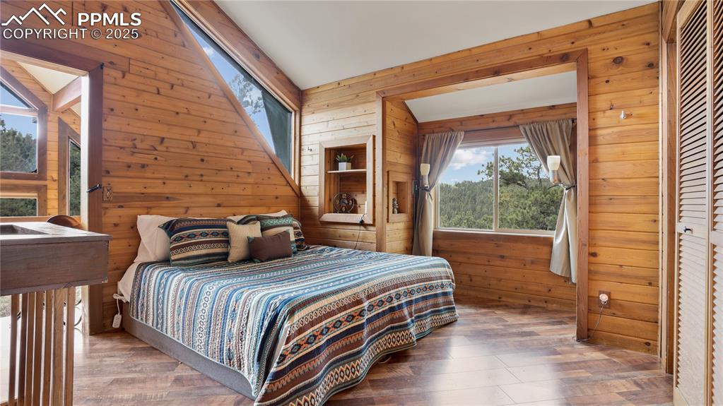 Bedroom featuring wooden walls, wood finished floors, and lofted ceiling