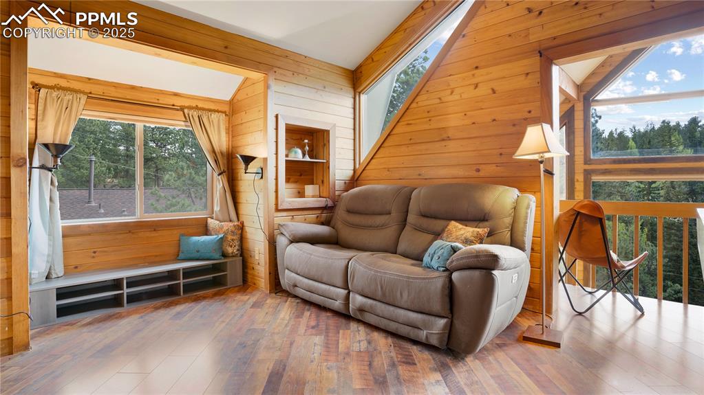 Living area with wooden walls, wood-type flooring, and vaulted ceiling
