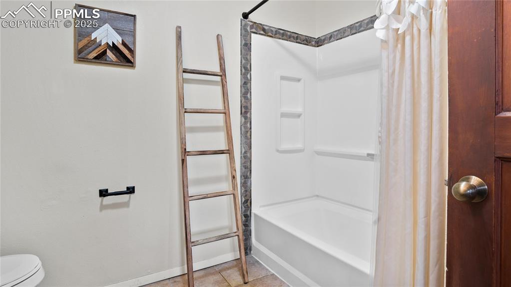 Full bathroom featuring shower / bath combo with shower curtain, toilet, baseboards, and tile patterned floors
