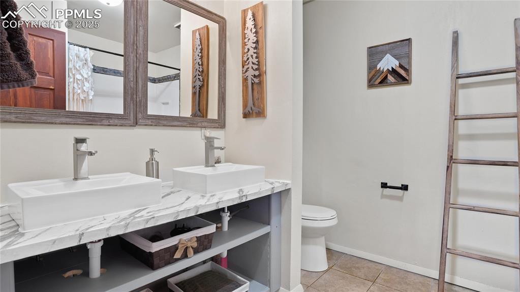 Full bath featuring toilet, tile patterned floors, baseboards, and double vanity