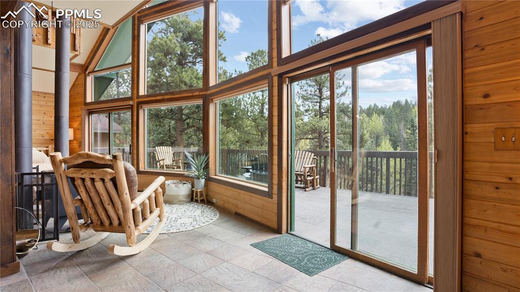 Sunroom / solarium featuring wooden walls, plenty of natural light, and a high ceiling