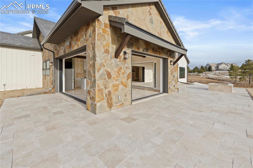 Back of property featuring a patio area, a shingled roof, and stone siding