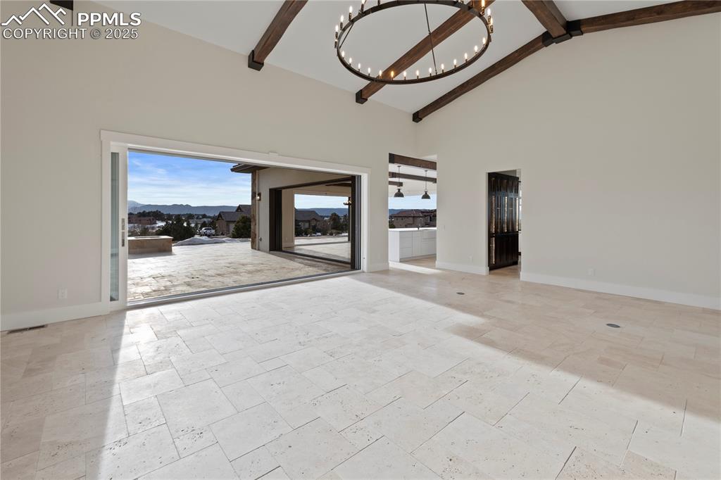 Unfurnished living room featuring baseboards, high vaulted ceiling, a chandelier, and beam ceiling