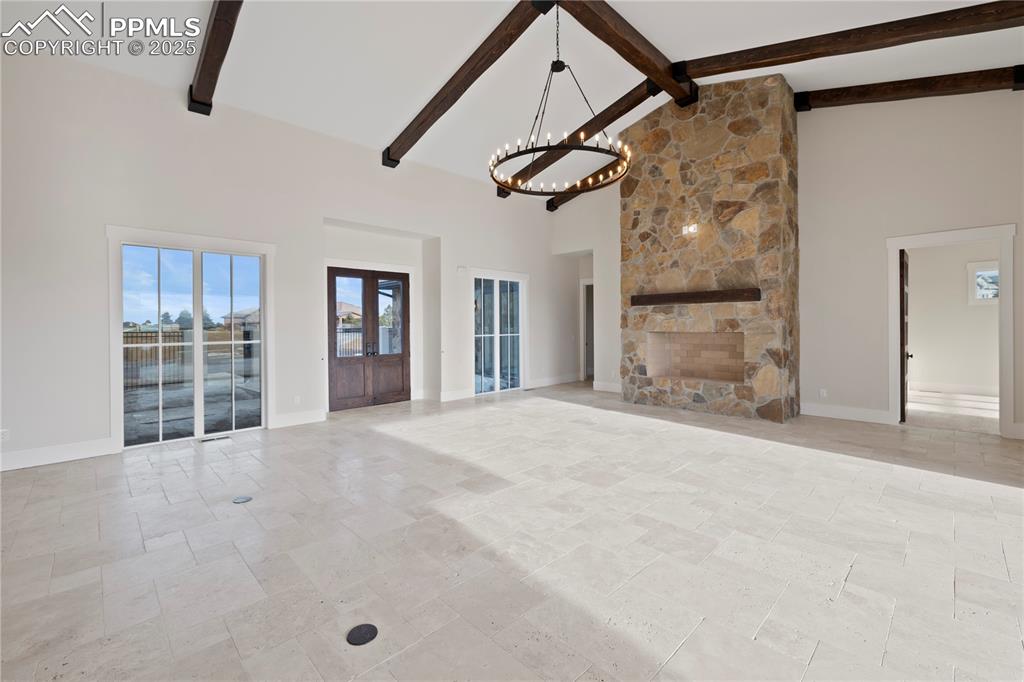 Unfurnished living room with high vaulted ceiling, a chandelier, beamed ceiling, stone finish flooring, and baseboards