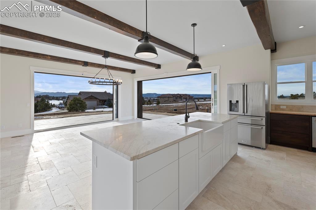 Kitchen with white cabinets, stone tile flooring, a sink, stainless steel refrigerator with ice dispenser, and light stone counters