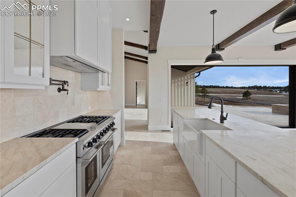 Kitchen featuring a sink, double oven range, tasteful backsplash, light stone countertops, and beamed ceiling