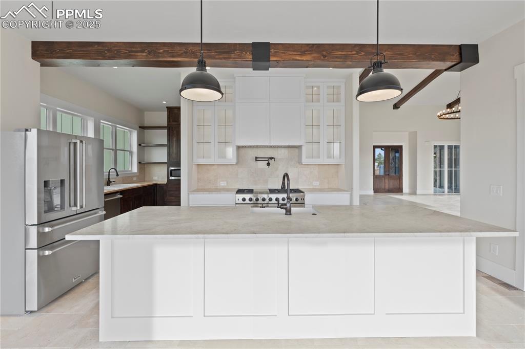 Kitchen with stainless steel appliances, beam ceiling, white cabinetry, a sink, and backsplash