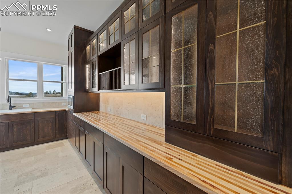 Kitchen featuring wood counters, recessed lighting, dark brown cabinetry, glass insert cabinets, and a sink