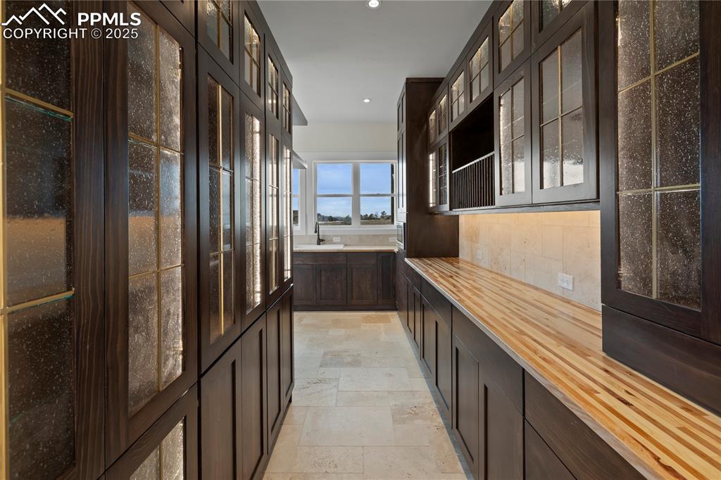 Kitchen with dark brown cabinetry, stone tile floors, wooden counters, glass insert cabinets, and recessed lighting