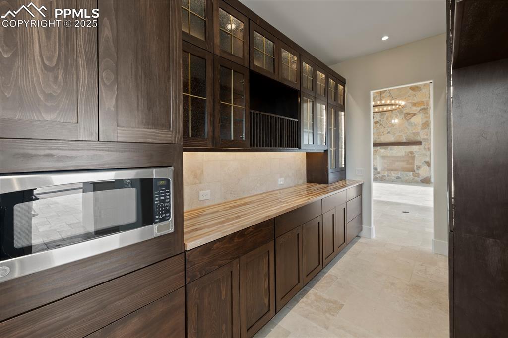 Kitchen with a chandelier, dark brown cabinetry, butcher block countertops, and stainless steel microwave