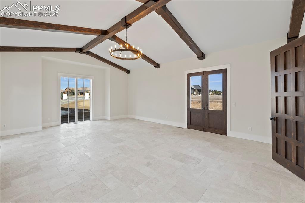 Unfurnished living room with vaulted ceiling with beams, stone tile floors, baseboards, and an inviting chandelier