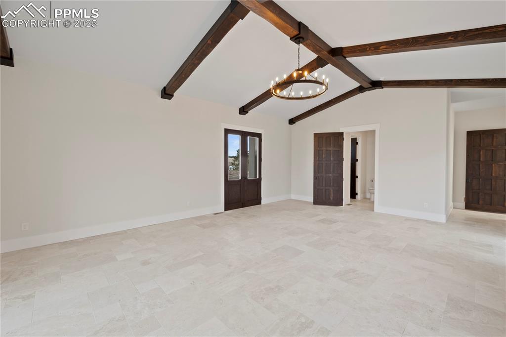 Unfurnished living room featuring lofted ceiling with beams, baseboards, and a chandelier