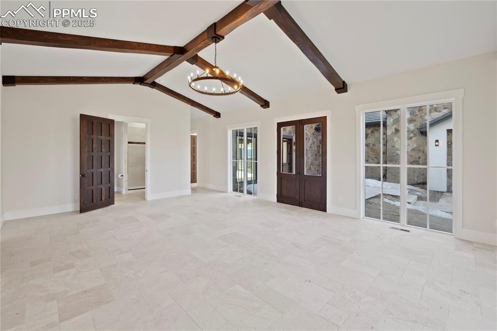 Unfurnished living room with lofted ceiling with beams, a notable chandelier, and baseboards