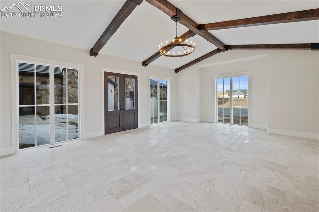 Spare room with lofted ceiling with beams, visible vents, baseboards, stone tile flooring, and a notable chandelier