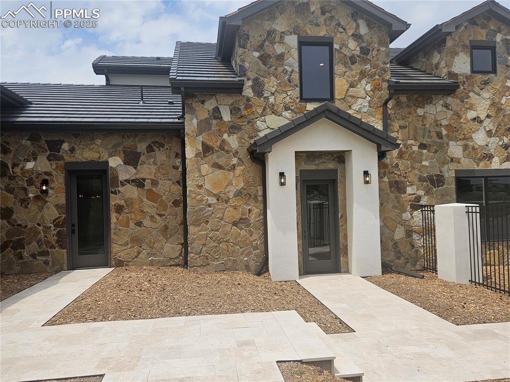 View of exterior entry with stone siding, a tile roof, and stucco siding