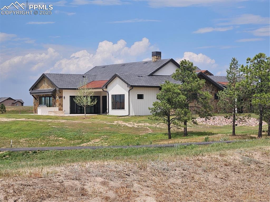 Back of house with a tile roof, a chimney, a lawn, and stone siding