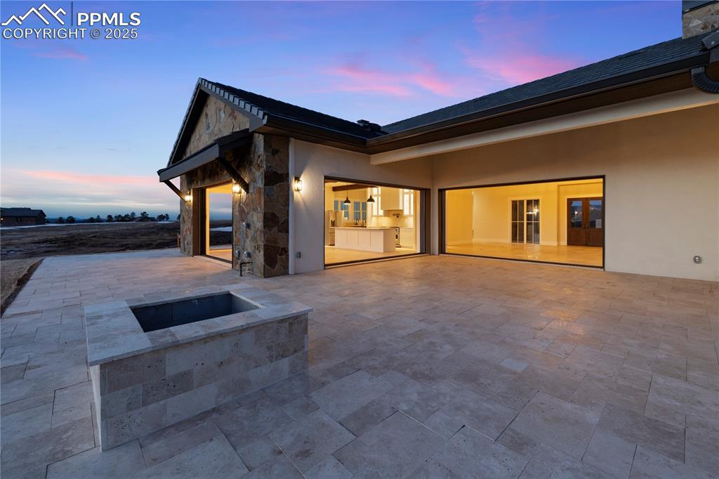 Back of house with stucco siding, a patio, and stone siding