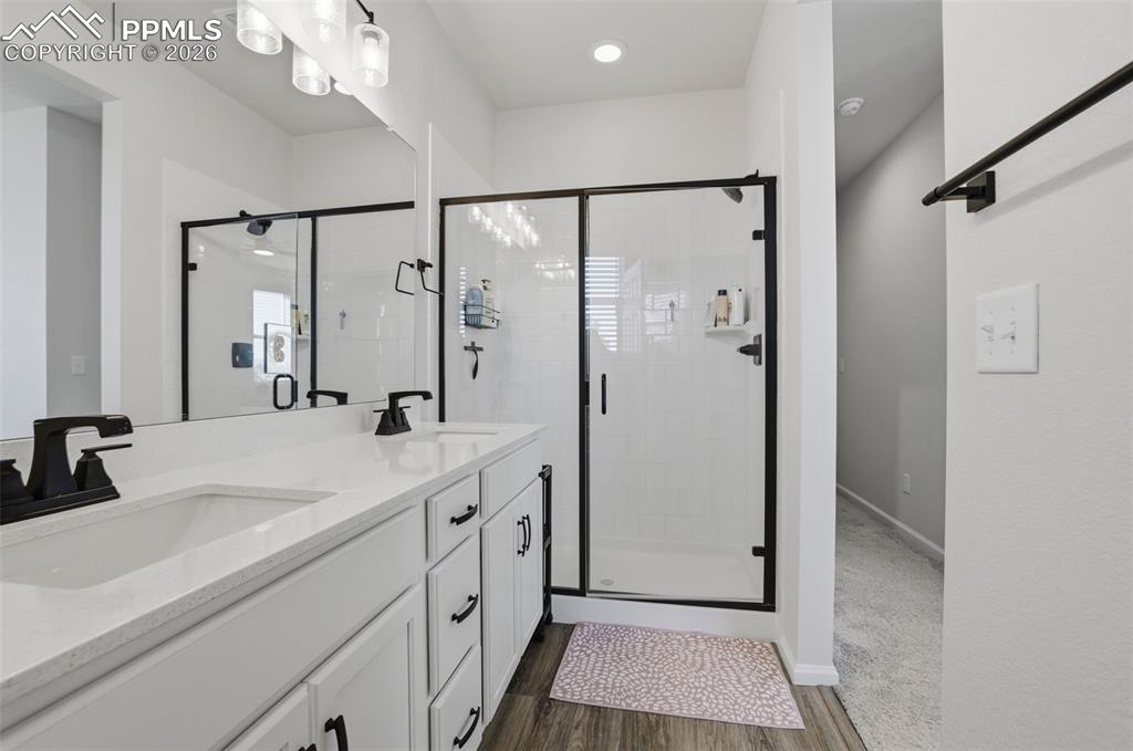 Bathroom featuring double vanity, a stall shower, and dark wood-type flooring