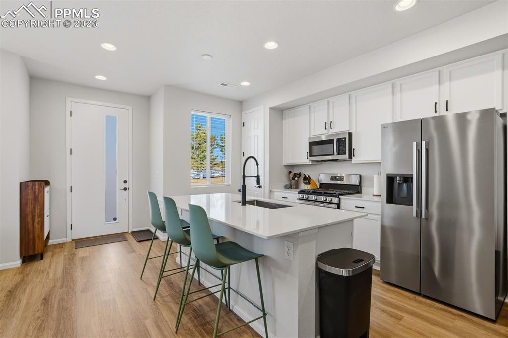 Kitchen featuring stainless steel appliances, white cabinetry, recessed lighting, a kitchen island with sink, and light wood finished floors