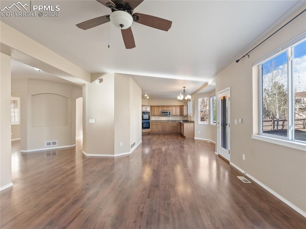 Unfurnished living room featuring ceiling fan, a chandelier, dark wood-style flooring, and arched walkways