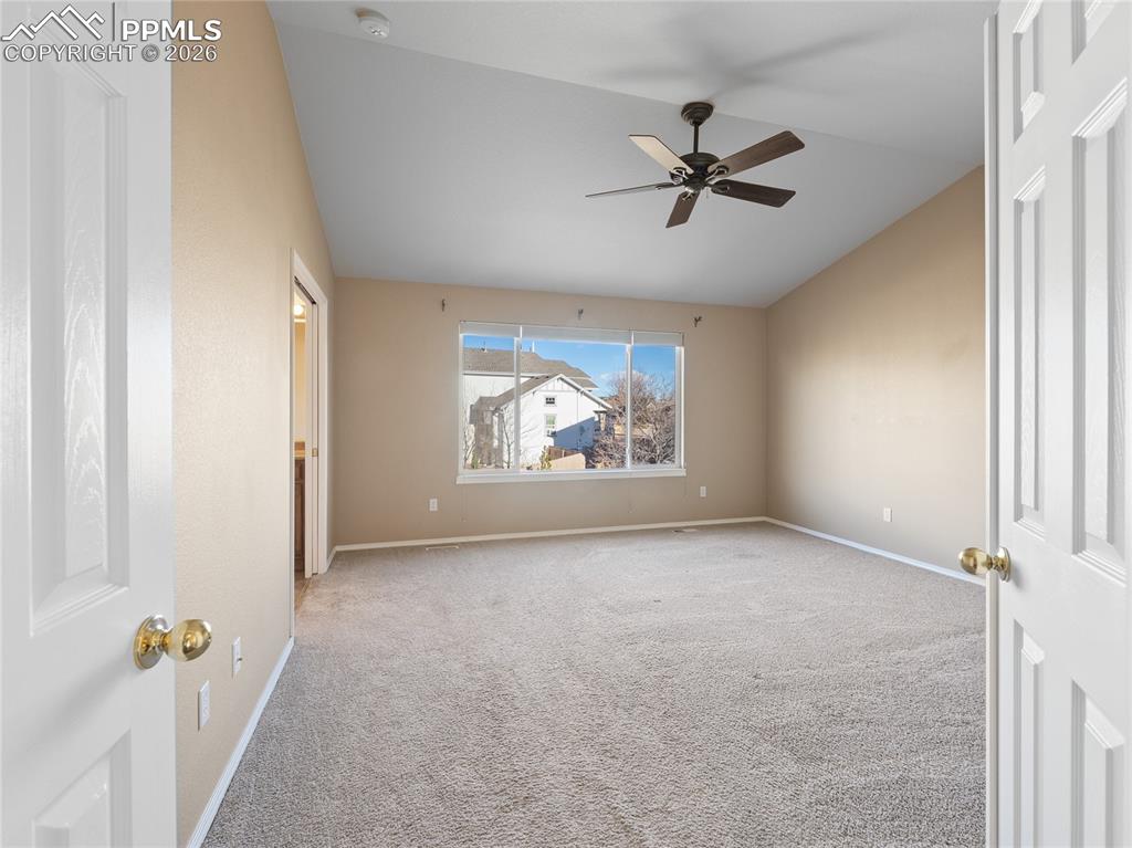 Carpeted primary bedroom featuring vaulted ceiling and ceiling fan