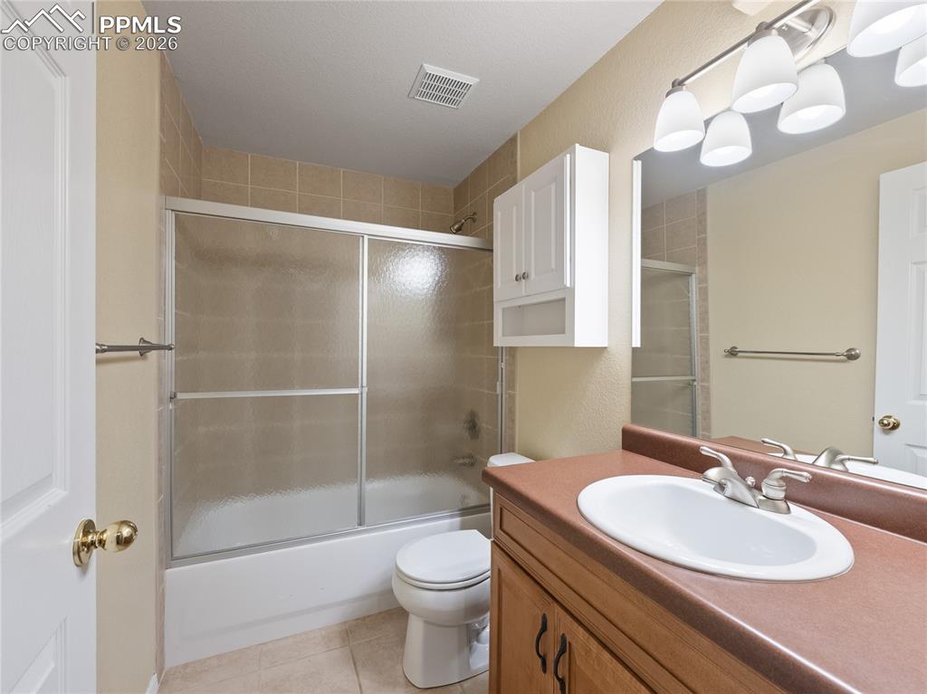 Full bathroom in basement featuring vanity, enclosed tub / shower combo, and light tile patterned floors