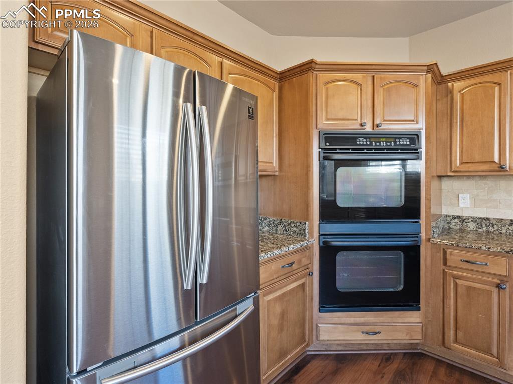 Kitchen with freestanding refrigerator, light stone countertops, dark wood finished floors, and wood finish cabinets