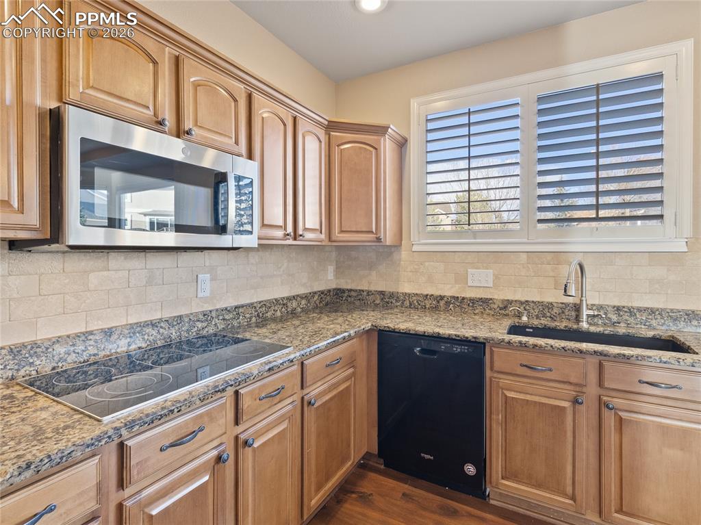 Kitchen featuring appliances, dark stone counters, and tasteful backsplash