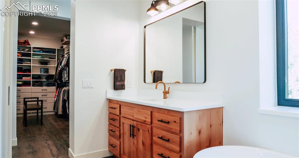 Full bathroom featuring a walk in closet, vanity, a freestanding bath, recessed lighting, and dark wood-style floors