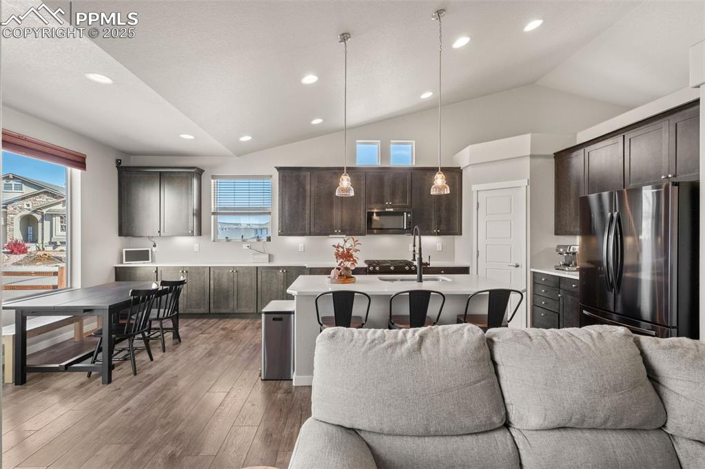 Kitchen featuring open floor plan, appliances with stainless steel finishes, a center island with sink, pendant lighting, and a kitchen breakfast bar