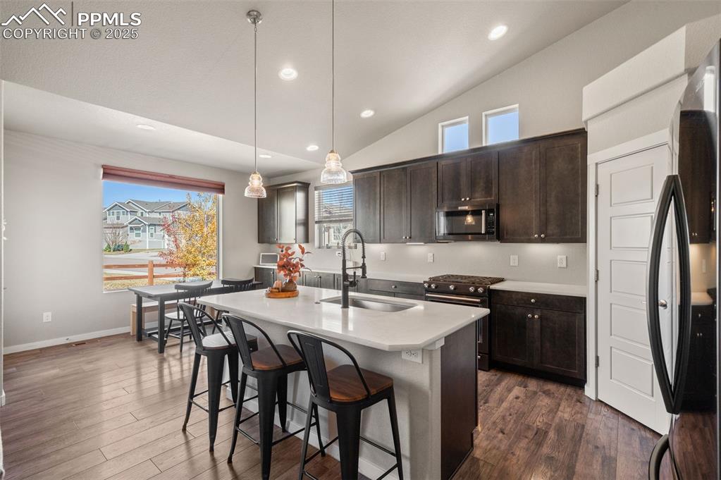 Kitchen featuring lofted ceiling, freestanding refrigerator, dark brown cabinets, recessed lighting, and decorative light fixtures