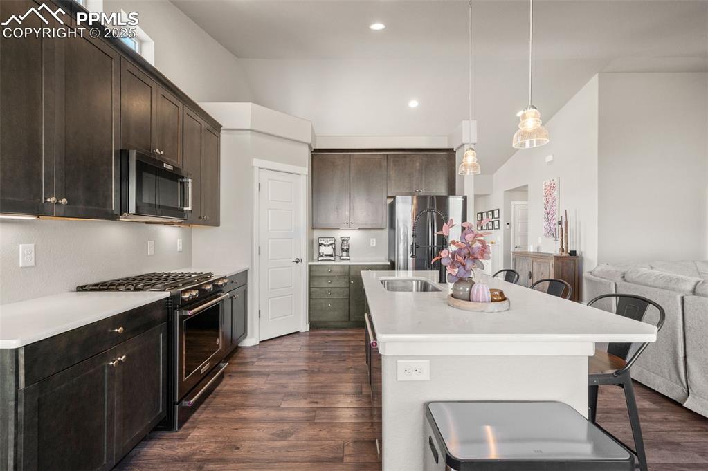 Kitchen with gas range, dark wood-type flooring, a kitchen breakfast bar, dark brown cabinets, and recessed lighting