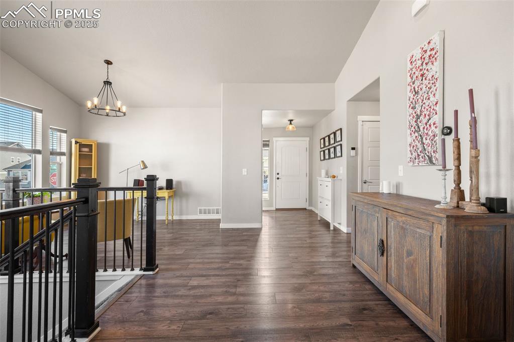 Foyer entrance with dark wood-style flooring, a chandelier, and vaulted ceiling