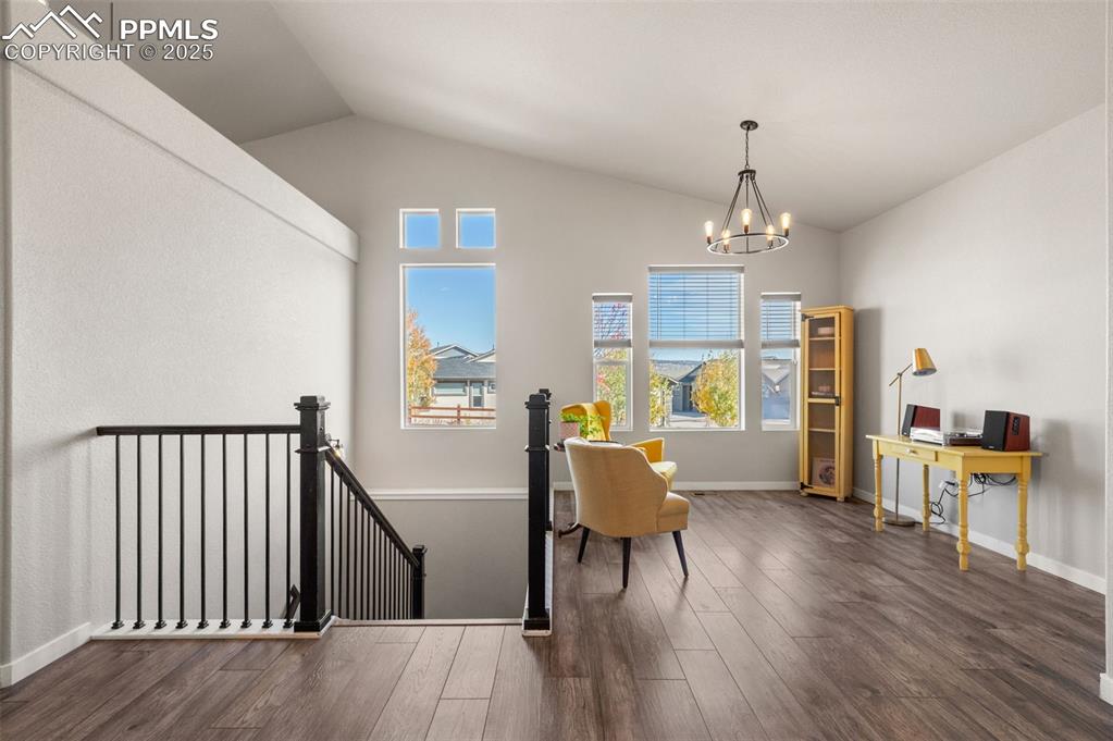 Living area featuring an upstairs landing, dark wood-style floors, lofted ceiling, and a chandelier