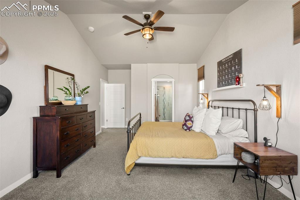 Carpeted bedroom featuring vaulted ceiling, ensuite bathroom, and ceiling fan