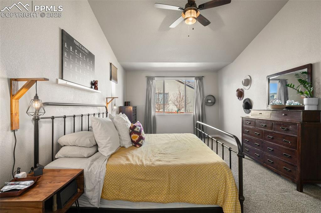 Carpeted bedroom with a ceiling fan and vaulted ceiling