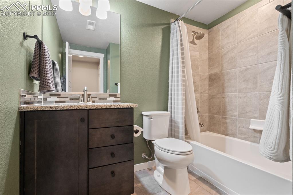 Full bath featuring a textured wall, shower / bath combination with curtain, vanity, and light tile patterned flooring