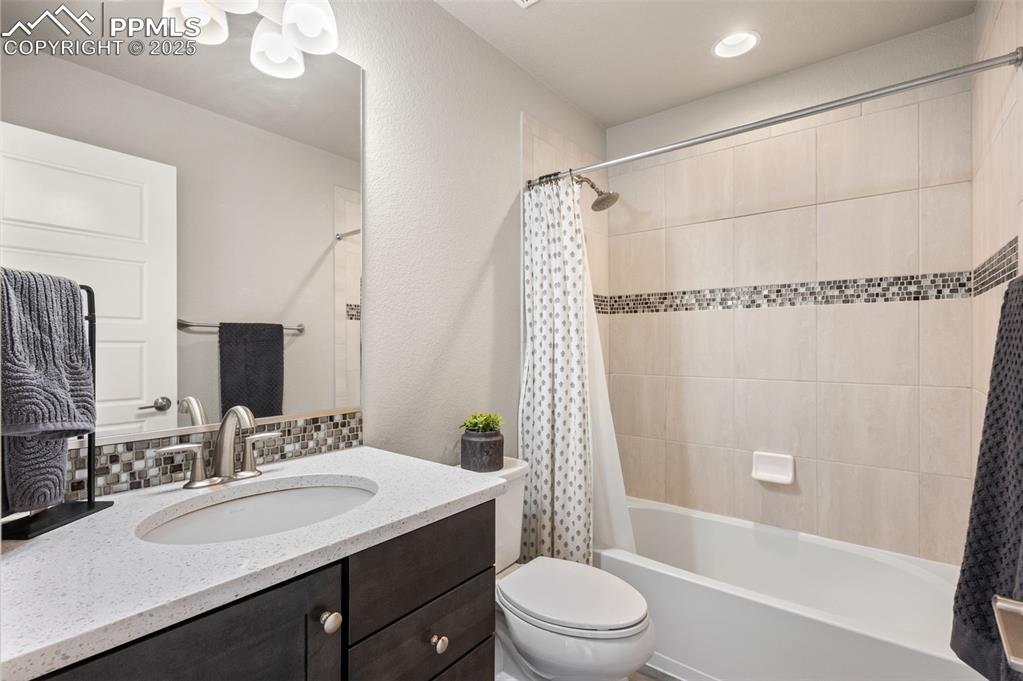 Full bathroom featuring vanity, shower / tub combo with curtain, a textured wall, and decorative backsplash