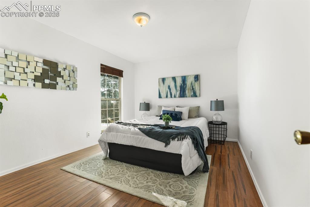 Upper Level Primary Bedroom with wood laminate floor and view window with window blinds.